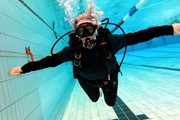 A woman in black diving gear swims underwater in a pool